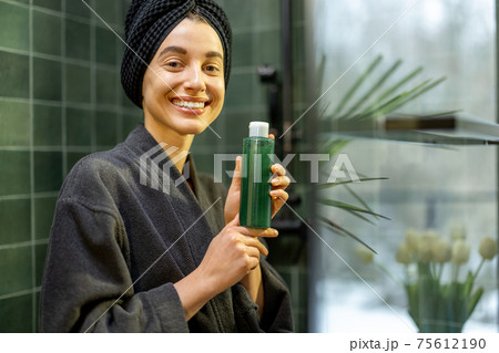 Woman holding a bottle with shampoo in bathroom 75612190