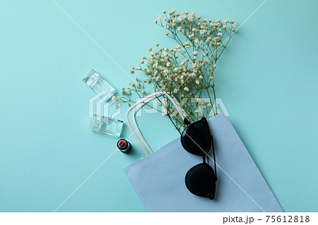 Bag, sunglasses, perfumes, lipstick and flowers on blue background Bag, sunglasses, perfumes, lipstick and flowers on blue background 75612818