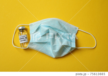 Vial of Covid - 19 vaccine and mask on yellow background 75613665