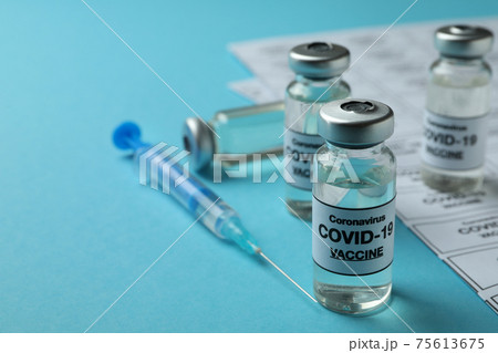 Concept of Covid - 19 vaccination with vials and syringe on blue background 75613675