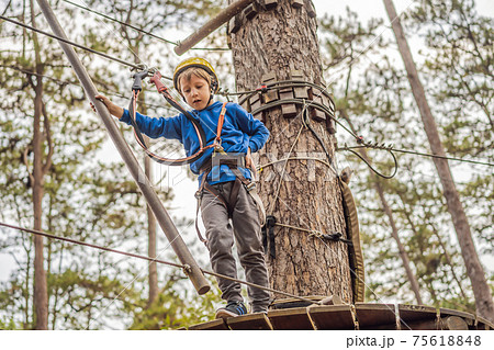 Happy child in a helmet, healthy teenager school boy enjoying activity in a climbing adventure park on a summer day Happy child in a helmet, healthy teenager school boy enjoying activity in a climbing adventure park on a summer day 75618848