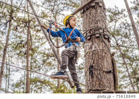 Happy child in a helmet, healthy teenager school boy enjoying activity in a climbing adventure park on a summer day Happy child in a helmet, healthy teenager school boy enjoying activity in a climbing adventure park on a summer day 75618849