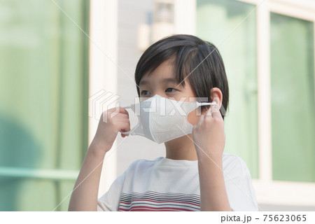 Asian child puts a safety mask on his face by himself Asian child puts a safety mask on his face by himself 75623065