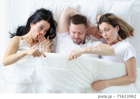 Two women and one man lie on bed in bedroom Two women and one man lie on bed in bedroom 75623962