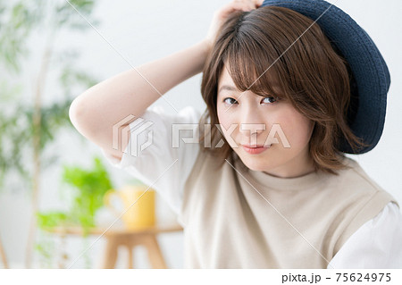 リビングで青い麦わら帽子をかぶろうとする若い女性のポートレート 75624975