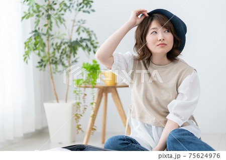 リビングで青い麦わら帽子をかぶろうとする若い女性のポートレート リビングで青い麦わら帽子をかぶろうとする若い女性のポートレート 75624976