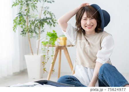 リビングで青い麦わら帽子をかぶろうとする若い女性のポートレート 75624977