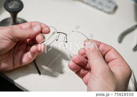 A man repairs a broken eyeglass frame. Close-up of the ophthalmologist's hands A man repairs a broken eyeglass frame. Close-up of the ophthalmologist's hands 75628550