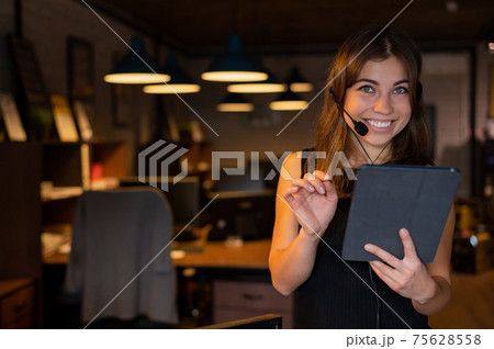 Beautiful business woman wearing in a headset is holding a digital tablet in the office 75628558