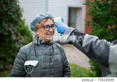 The doctor measures the temperature of an elderly woman with a non-contact infrared thermometer outdoors The doctor measures the temperature of an elderly woman with a non-contact infrared thermometer outdoors 75628999