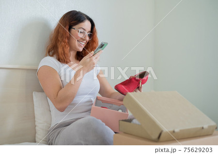 The woman unpacks the delivered shoes. The girl leaves a review about the order in the application on the smartphone 75629203
