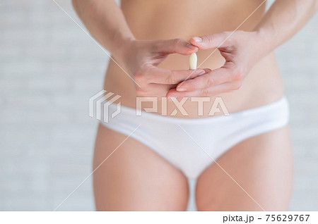 Faceless Caucasian woman in white panties and with a bare belly holds a healing candle. Girl demonstrates anal or vaginal suppository. Prescription from a gynecologist for women's health. 75629767