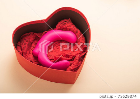 Clitoral vaginal vibrator and lace red women's panties in a box in the form of a heart on a cream background Clitoral vaginal vibrator and lace red women's panties in a box in the form of a heart on a cream background 75629874