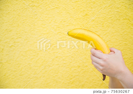 Female hands hold a banana on a yellow background 75630267