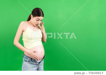 pregnant woman in unzipped jeans showing her naked abdomen at colorful background with copy space 75630917