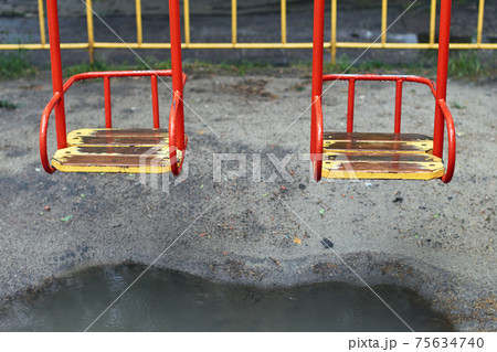 Metal swing with a wooden seat on a kids playground on a rainy day with a puddle under it 75634740