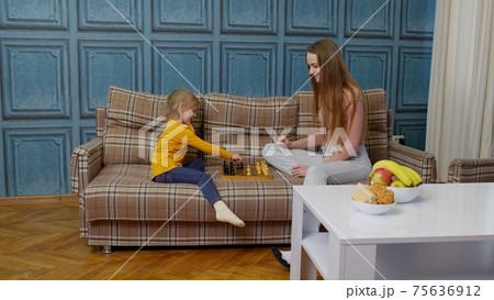 Small cute daughter child and young mother playing chess at home sofa, leisure hobbies activities Small cute daughter child and young mother playing chess at home sofa, leisure hobbies activities 75636912
