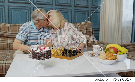 Retired senior couple talking drinking tea, playing chess in modern living home room lounge together Retired senior couple talking drinking tea, playing chess in modern living home room lounge together 75636917