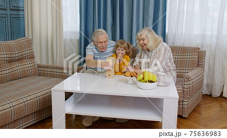 Senior couple grandparents and granddaughter enjoying board game building tower from blocks at home Senior couple grandparents and granddaughter enjoying board game building tower from blocks at home 75636983