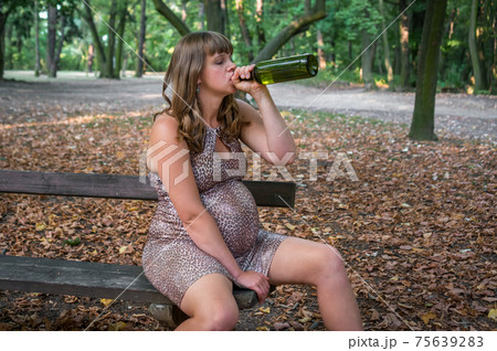 Pregnant woman drinking wine in the park - alcoholism concept Pregnant woman drinking wine in the park - alcoholism concept 75639283