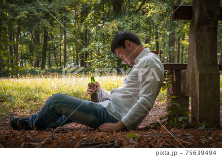 Drunk man lies on the ground near bench with a beer bottle Drunk man lies on the ground near bench with a beer bottle 75639494
