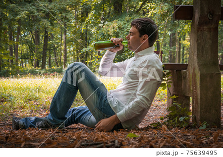 Drunk man lies on the ground near bench with a beer bottle Drunk man lies on the ground near bench with a beer bottle 75639495
