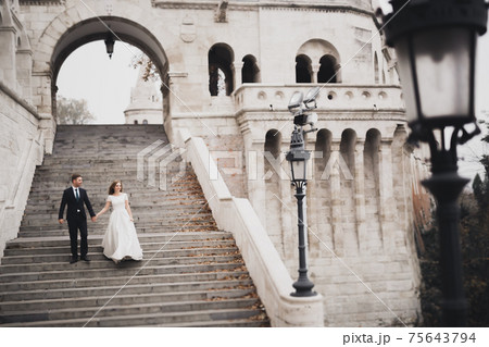 Beautiful wedding couple climbing up a gorgeous stairs holding hands and looks to each other 75643794
