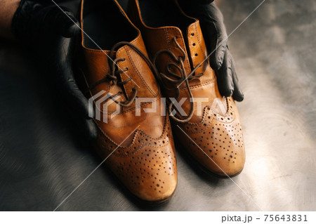Close-up top view of hands of shoemaker shoemaker in black gloves holding old worn light brown leather shoes 75643831