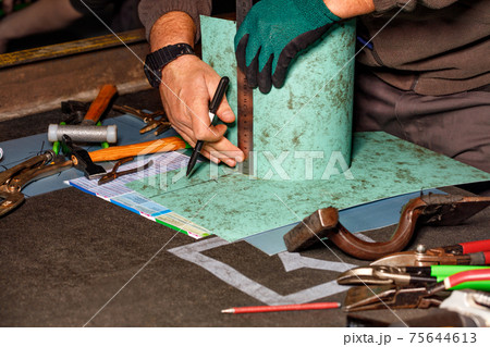The tinsmith in his workshop marks the required size on the workpiece with a felt-tip pen and a ruler. 75644613
