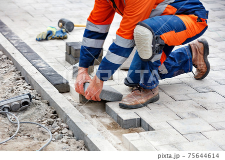 The hands of a working bricklayer are laying paving slabs during the spring day. 75644614