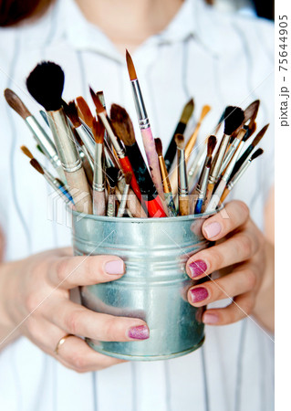 Professional artist's brushes in an iron bucket in women's hand with pink manicure. The concept of creativity and painting. Professional artist's brushes in an iron bucket in women's hand with pink manicure. The concept of creativity and painting. 75644905