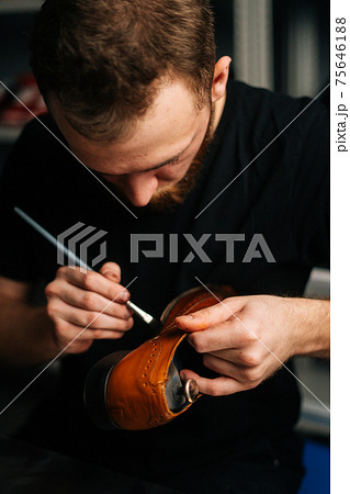 Portrait of shoemaker painting heel and sole of light brown leather shoes with brush 75646188
