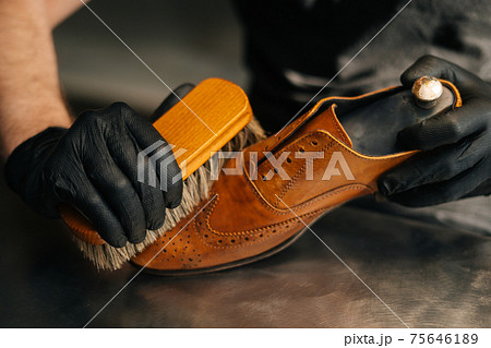 Close-up hands of unrecognizable shoemaker cleaning with brush old light brown leather shoes. Close-up hands of unrecognizable shoemaker cleaning with brush old light brown leather shoes. 75646189