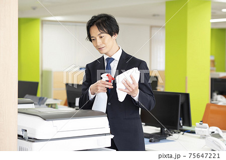 会社で共用のコピー機(複合機)の除菌掃除をする男性 75647221