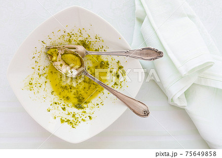 Closeup of eaten linguine pasta plate with pesto genovese, cutlery and napkin Closeup of eaten linguine pasta plate with pesto genovese, cutlery and napkin 75649858