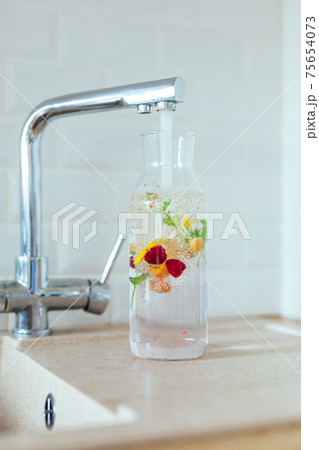 Filling a clear glass carafe with tap water. Water is infused with berries, mint and lemon 75654073