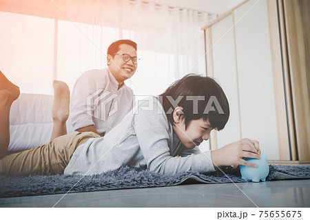 Happy Father is watching his son making money saving by inserting coin into a blue piggy bank in bedroom for Financial Education concept. 75655675