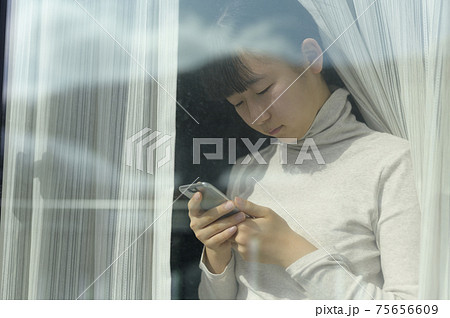 窓辺でスマートフォンを見る女の子(外出自粛要請のイメージ) 窓辺でスマートフォンを見る女の子(外出自粛要請のイメージ) 75656609
