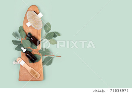 Essential oils and massage brushes with natural eucalyptus leaves on green background. Beauty products, massage tools, facial skin care, spa beauty treatment concept. Flat lay, copy space 75658975