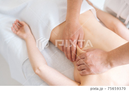 Male masseur massaging back of young woman lying on massage table. Concept of massage spa treatments 75659370
