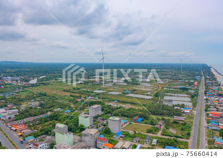Aerial view of wind turbine with residential buildings in Nakhon Si Thammarat with sea skyline, Thailand. Urban town city in Asia. Architecture landscape background. Aerial view of wind turbine with residential buildings in Nakhon Si Thammarat with sea skyline, Thailand. Urban town city in Asia. Architecture landscape background. 75660414