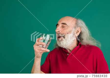Senior grey-haired man with glass of water isolated over green background. Senior grey-haired man with glass of water isolated over green background. 75663430