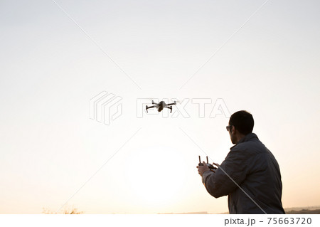 A man launches a drone into the sky. Drone operator with setting sun. A man launches a drone into the sky. Drone operator with setting sun. 75663720
