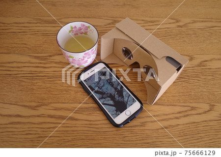 ダンボール製vrゴーグルと桜の木が映ったスマホ画面と緑茶の写真素材