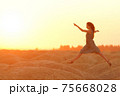 Elegant woman in long dress with straw hat junping elegant on sandy hills in desert. Sunrise, backlight photo 75668028
