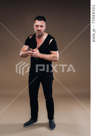 Against a gray background stands a battered angry man in a black T-shirt with wounds 75668301