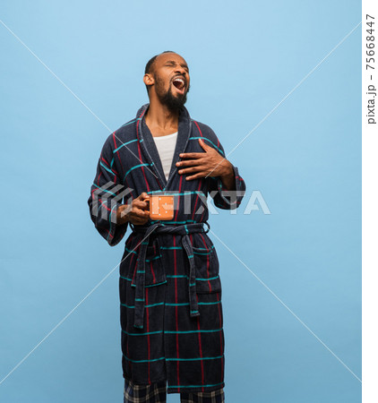 African-American man in bathrobe with cup of coffee isolated on blue background African-American man in bathrobe with cup of coffee isolated on blue background 75668447