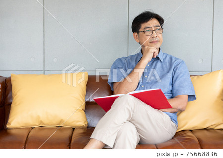 senior asian man reading book and thinking something on sofa senior asian man reading book and thinking something on sofa 75668836