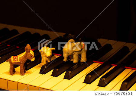 グランドピアノの鍵盤の上に置いたロバ、ゾウ、ヒツジの置物 75670351
