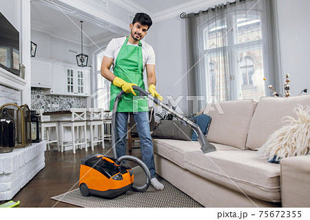 Indian guy in uniform cleaning couch with modern vacuum 75672355